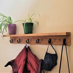 a coat rack with three coats hanging on it and two potted plants in the background