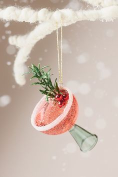 a christmas ornament hanging from a branch with snow falling on it and mist