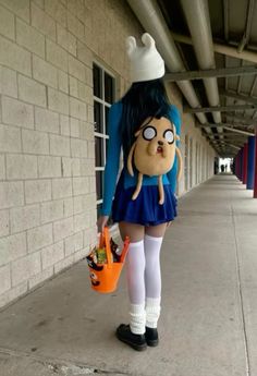 a woman in a blue dress and white hat holding an orange bag while standing next to a building