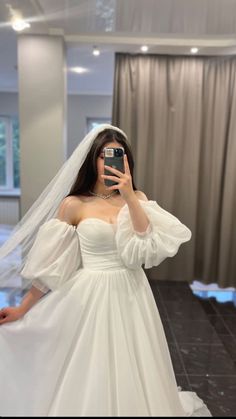 a woman in a wedding dress taking a selfie with her cell phone while wearing a veil