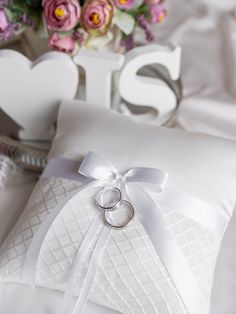 two wedding rings are tied to a pillow on a bed with flowers in the background