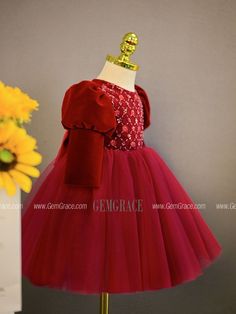 a red dress on display with sunflowers in the background and an orange vase behind it