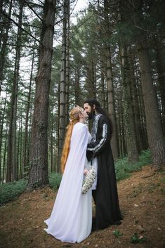 a man and woman dressed in medieval clothing standing next to each other near some trees