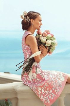 a woman sitting on a ledge with flowers in her hand