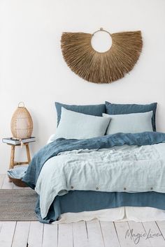 a bed with blue sheets and pillows in a room next to a wicker wall decoration