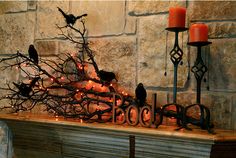 a fireplace mantle decorated with candles, branches and birds on the mantelpieces