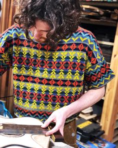 a man with long hair is working on a piece of wood in his workshop,