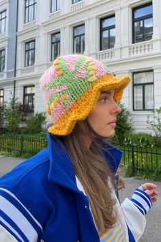 a woman wearing a knitted hat with flowers on the brim and in front of a large white building