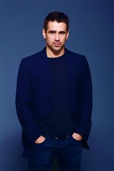 a man standing in front of a blue wall with his hands in his pockets and looking at the camera