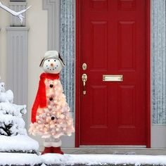 a snowman is standing next to a red door in front of a white christmas tree