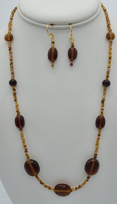 This simple brown beaded necklace was made with brown seed beads and round oblong brown glass beads.  The 22 inch necklace has a 14 K gold plated lobster claw clasp.  The matching earrings are made from the same brown beads as the necklace .  The earrings hang a total of 1 1/2 inches in length and have a 14 K gold plated earring wire. Brown Beaded Necklaces With Oval Beads, Brown Beaded Necklace With Oval Beads, Brown Beaded Necklace With Colorful Oval Beads, Elegant Brown Polished Beads, Elegant Brown Polished Beaded Necklace, Brown Necklaces With Colorful Oval Beads, Elegant Brown Beaded Necklace With Polished Beads, Brown Necklaces With Polished Oval Beads, Brown Czech Glass Beaded Jewelry