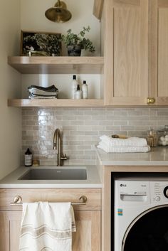 a washer and dryer in a small room with wooden shelves above the sink