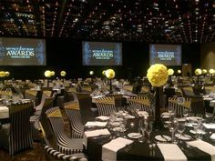 an empty banquet room with black and white tablecloths, yellow flowers and large screen screens