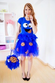 a woman in a blue dress holding a cookie monster bag and cookies on her hand