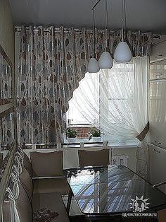 a dining room table and chairs in front of a window with curtains on the windowsill