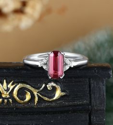 a close up of a ring with a red stone in the middle and two diamonds on it