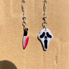 two pairs of earrings with black, white and pink designs hanging from hooks on brown paper