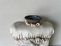 a ceramic bowl sitting on top of a white piece of art that is shaped like a tree stump