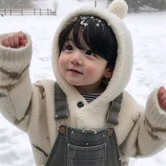 a small child wearing overalls and a hoodie in the snow with his hands up