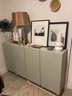 a sideboard with two pictures on it and a lamp in the corner next to it