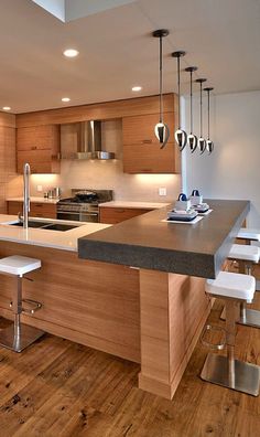 a kitchen with an island and stools in the center, surrounded by wood flooring