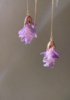 two purple flowers hanging from long gold chain necklaces with dangling earring hooks on grey background