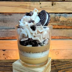 an ice cream sundae with oreo cookies and whipped cream in it on top of a wooden block