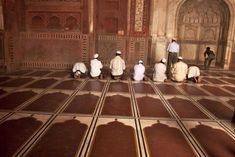 five men sitting on the floor in front of an ornate wall and doorway, all wearing white