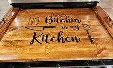 a wooden cutting board that says no bitchin in my kitchen on top of an oven