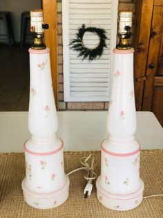 two white lamps sitting on top of a table next to a wreath with a door in the background