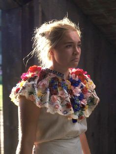 a woman wearing a white dress with colorful flowers on it's shoulders and neck