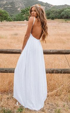 a woman standing in front of a fence wearing a white dress with back cutouts