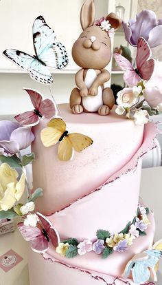 there is a pink cake with butterflies on it and a bunny sitting on the top