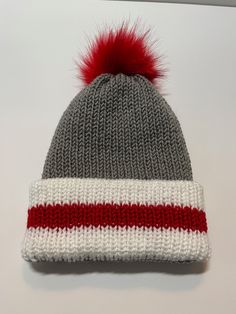 a knitted hat with a red and white stripe on the front, and a pom - pom at the top