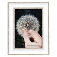 a dandelion in a white frame with a person's hand holding it