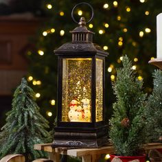 a lighted lantern with a snowman on it in front of christmas trees and lights