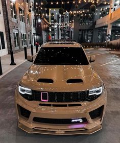 the front end of a tan car parked in a parking lot at night with lights on