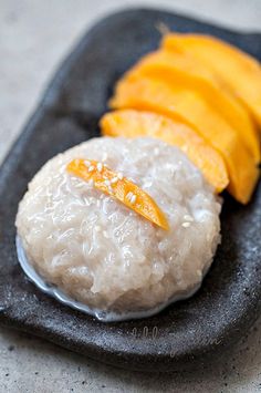 a black plate topped with rice and sliced up mangos on top of it's side