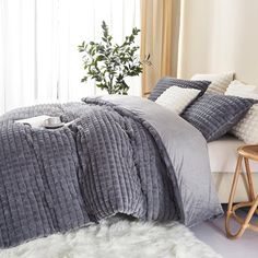 a bed with grey and white comforters in a bedroom next to a window,