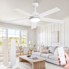 a person holding a remote control in front of a living room with white walls and furniture