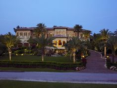 a large house with palm trees and landscaping in front of it at dusk or dawn