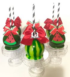 three watermelon covered candy apples with bows and candles in them are sitting on glass pedestals