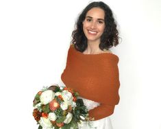 a woman holding a bouquet of flowers in her hands and smiling at the camera while standing against a white wall