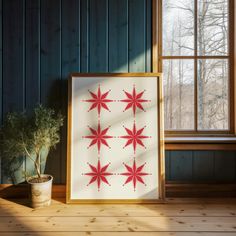 a potted plant sitting next to a framed art piece on a wooden floor in front of a window