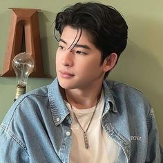 a young man wearing a denim jacket sitting in front of a wall with a light bulb on it