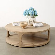 a coffee table with blue flowers in a vase and books on the top, next to a white wall