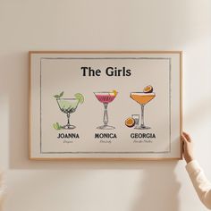 a woman holding up a framed poster with different cocktails on it's wall