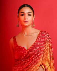 a woman in a red and yellow sari standing against a red wall with her hands on her hips