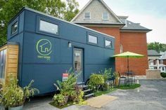 the tiny house is parked outside in front of some trees and plants with an umbrella