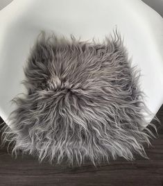 a white plate topped with a furry gray animal fur rug on top of a wooden floor